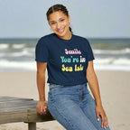 Person wearing a navy blue t-shirt with colorful text, sitting on a stool against a white background