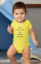 Baby wearing a yellow onesie with text, standing in front of a blue slide.