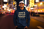 Man wearing a hoodie with 'men's mental health awareness' text on a city street at night.