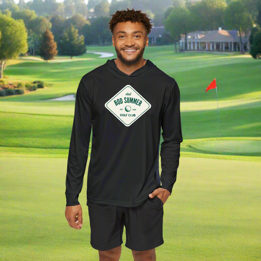 A man wearing a black golf performance hoodie with a text logo on the front standing on a golf course.